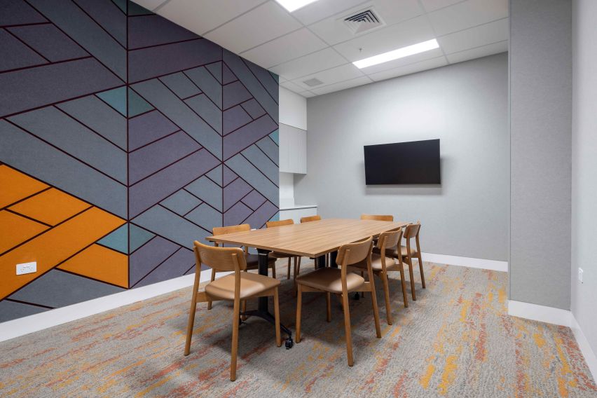 Small meeting room with a wooden table and 6 chairs in the centre, with a TV on the far wall.